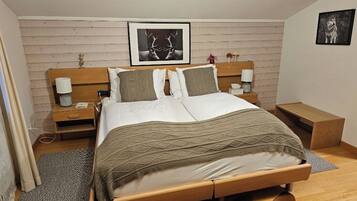 Un dormitorio ordenado con cabecera de madera, cama grande con manta estampada, dos mesitas de noche con lámparas y un cuadro enmarcado en la pared.