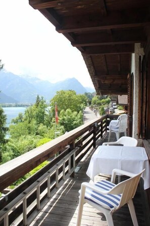 Una terraza de madera con una mesa y sillas, con vista a un lago y montañas.