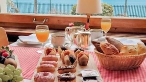 Un bufé de desayuno con diversos pasteles, frutas, queso y pan sobre una mesa, con vista a la montaña al fondo.