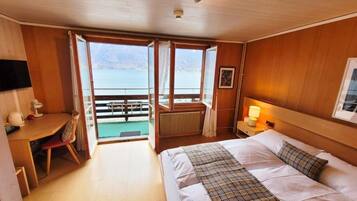 Quarto de hotel com cama, escrivaninha, cadeira, janela com vista para o mar e mesa de cabeceira com abajur.