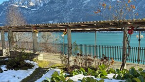 Un jardín con plantas cubiertas de nieve y un pergolado de madera con adornos colgantes.