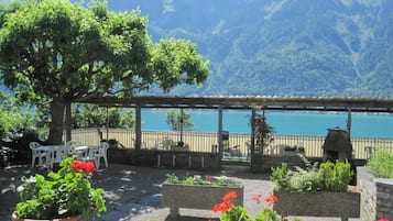 Una terraza con plantas en macetas, muebles de exterior y vistas a un lago y montañas.