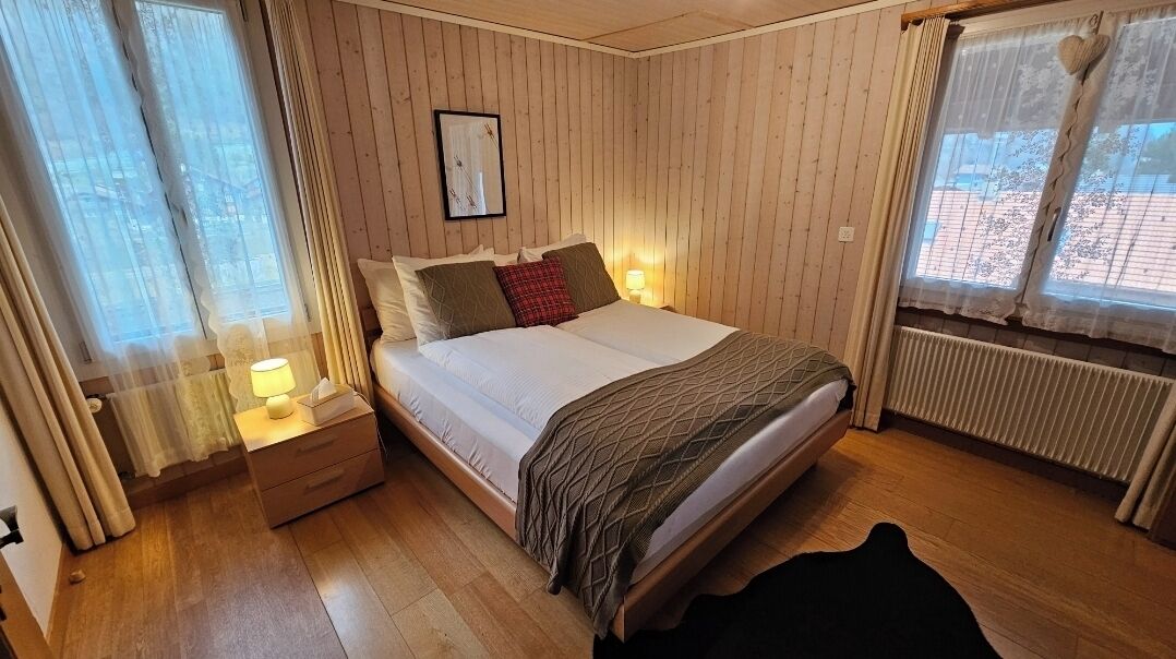 Un dormitorio con cama, mesitas de noche, una ventana con cortinas y un radiador.