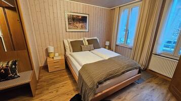 A bedroom with a bed, bedside tables, a chair, a window, and a wall-mounted picture.