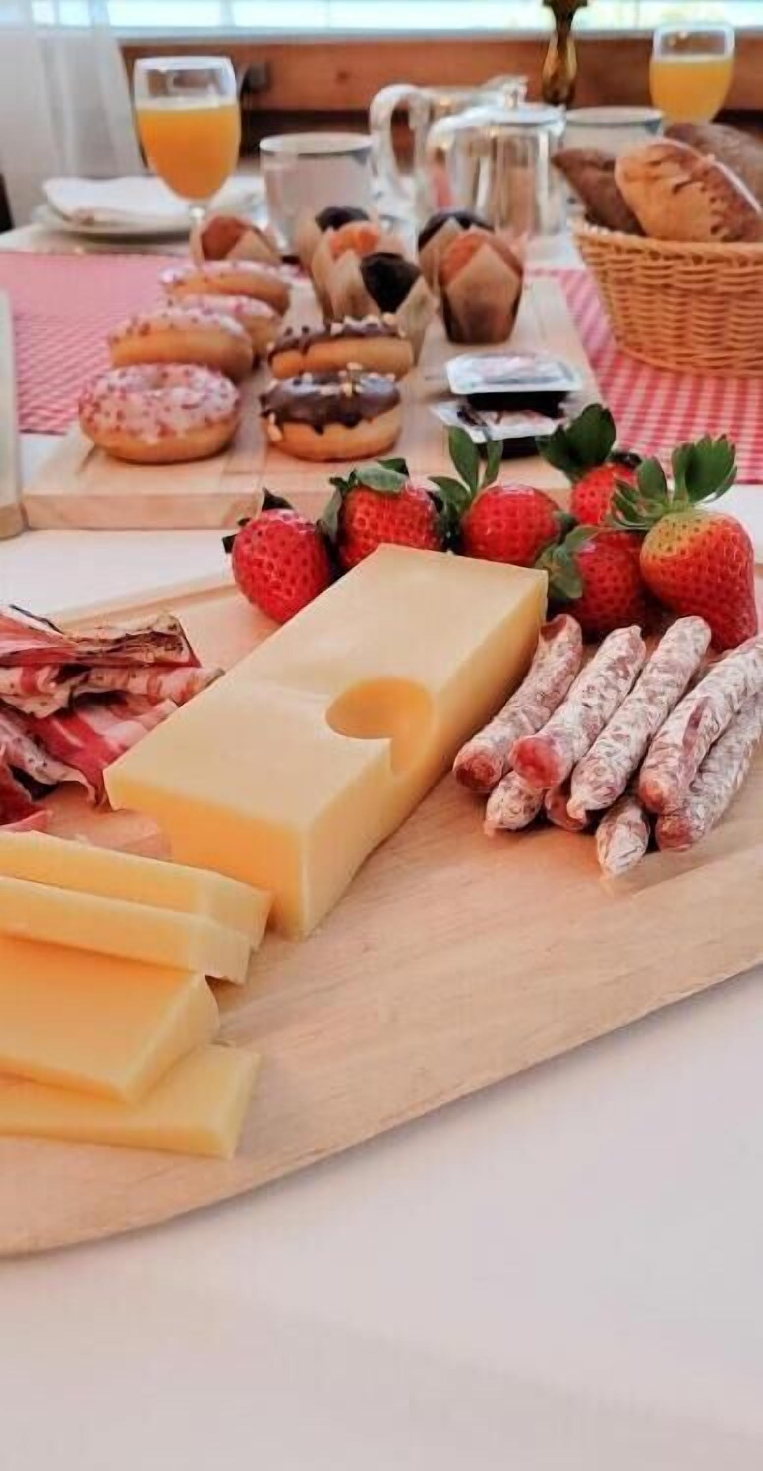 Una mesa de desayuno con queso, salchichas, fresas y pasteles sobre una tabla de madera.