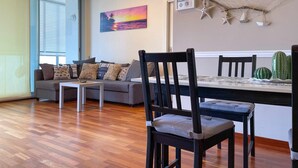 A modern living room with a sofa, a dining table, and chairs. There is a painting on the wall and a cactus on the table.