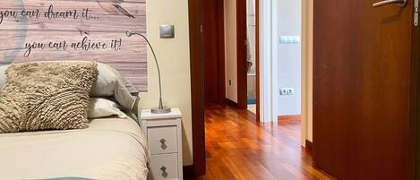 A bedroom with a bed, a bedside lamp, a wall art with motivational text, and a wooden floor.
