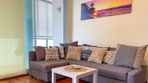 A living room with a grey sofa, multiple patterned cushions, a white coffee table, and a wooden floor.