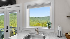 A kitchen with a stainless steel sink, white cabinets, a window with a view of green hills, and a flat-screen TV mounted above the sink. - "New Listing" Private Romantic Guest Loft with a VIEW! (Marion)
