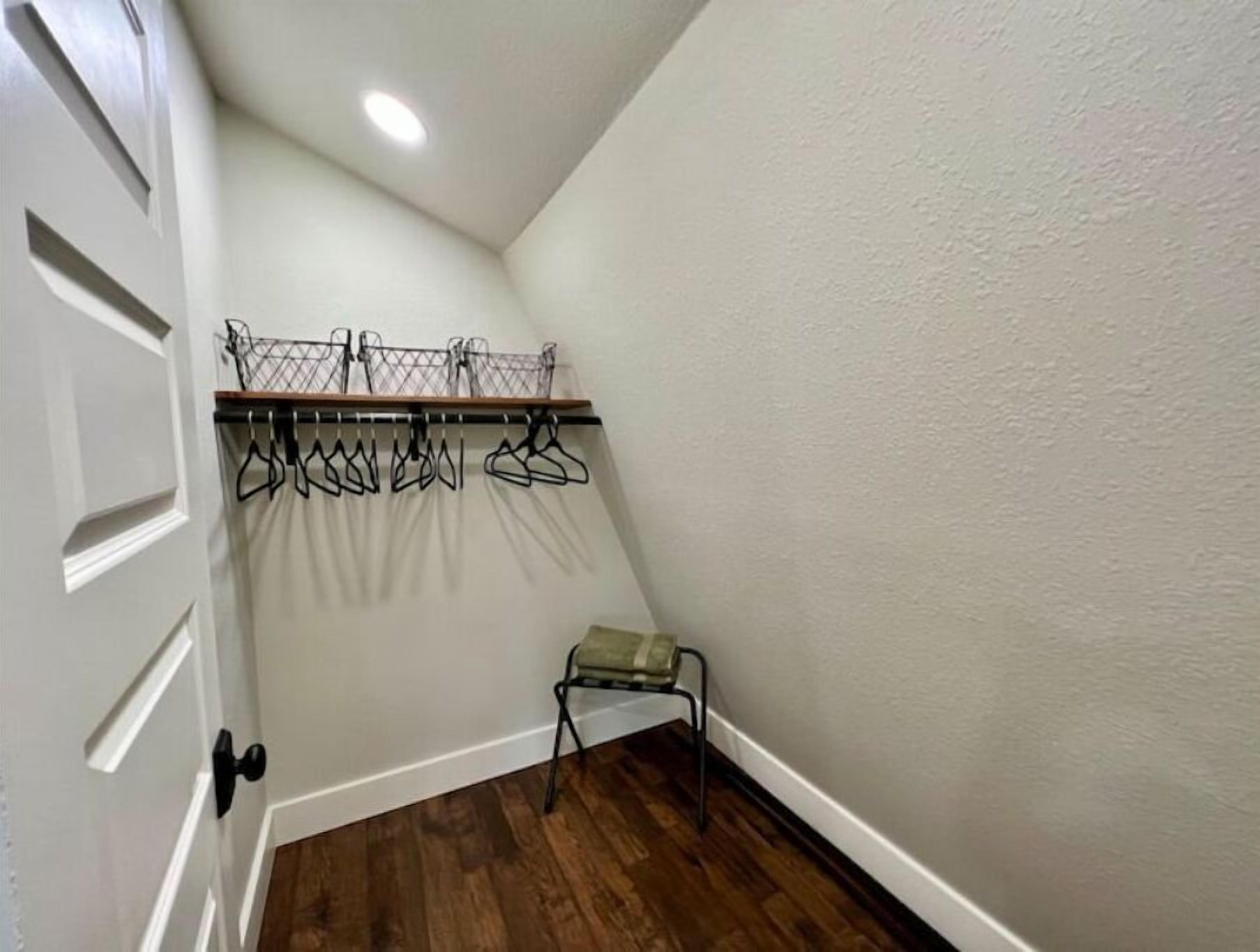 Ein Eckzimmer mit Holzboden, einer weißen Tür, einem kleinen Stuhl und einem Kleiderständer mit Kleiderbügeln.