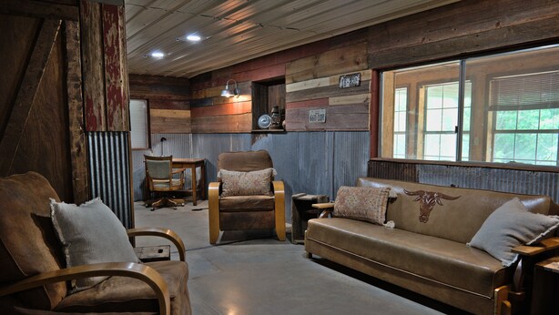A rustic interior with a leather sofa, wooden armchairs, and a wooden dining table. - T's Fish Camp--Crappie Are Biting—Sleeps up to Six (Warsaw)