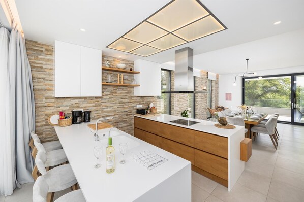 Cocina moderna con una isla central, armarios blancos y un salpicadero de piedra.