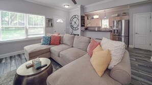 A modern living room with a sectional sofa, a round coffee table, and a ceiling fan. - 3-BR Getaway Near Center City/Plaza Midwood/NoDa! (Charlotte)