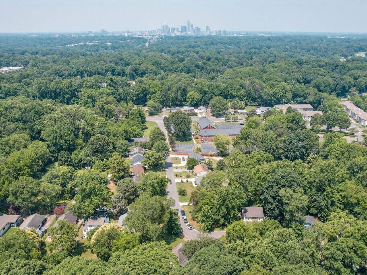 Vue aérienne d’un quartier résidentiel avec des maisons, des rues et, au loin, le profil urbain d’une ville.
