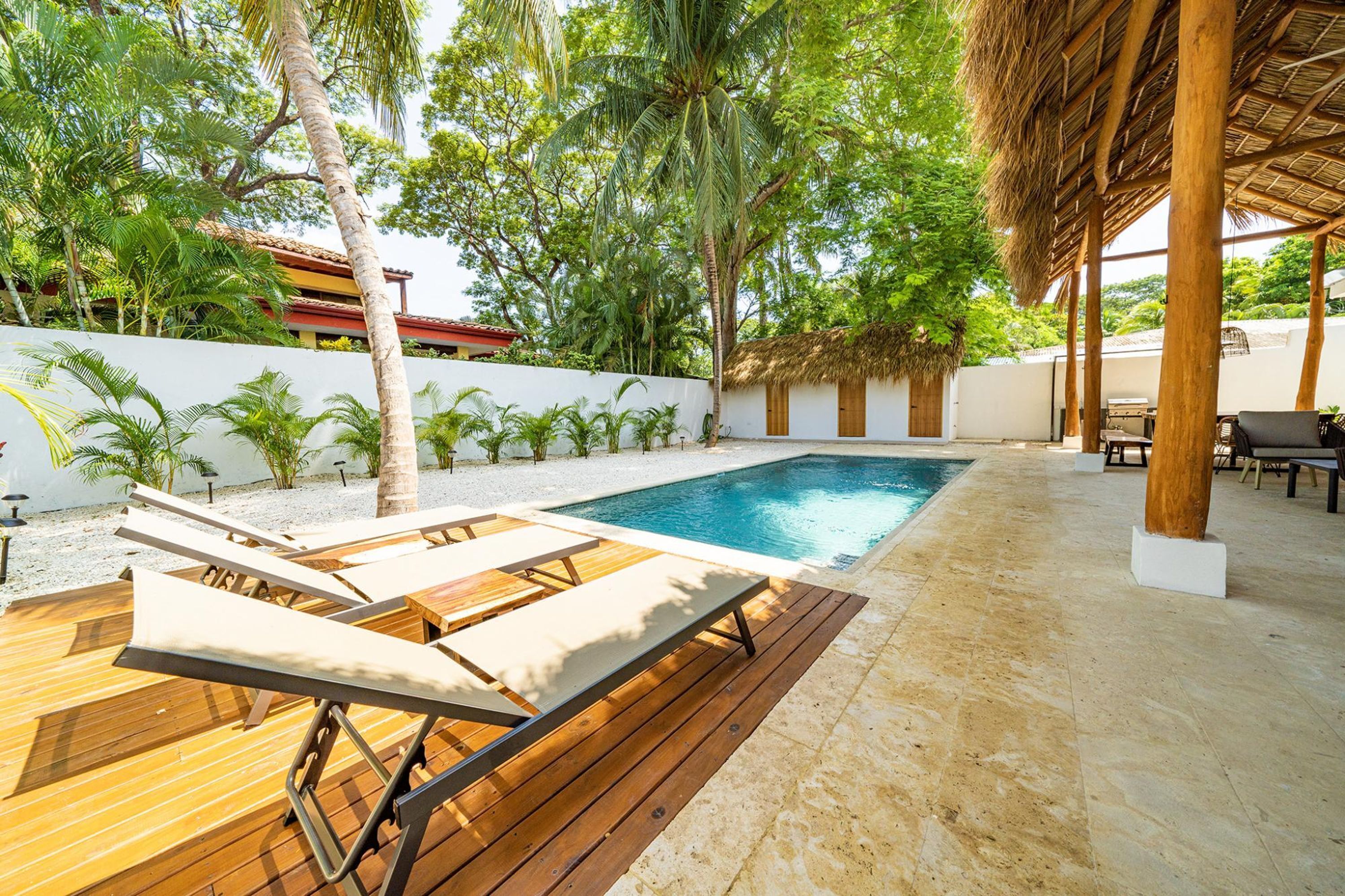 A pool area with wooden loungers, a thatched roof structure, and surrounding palm trees.
