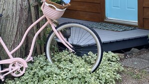 En lyserød cykel med en kurv fyldt med blomster parkeret ved siden af en træbygning med teksten "Potting Shed".