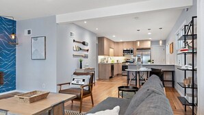 A modern living room with a sofa, a dining table, and a kitchen in the background. - Steps To Lake|Garage Parking|Fire Table|Deck|Bikes (Minneapolis)