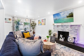 A modern living room with a fireplace, a large TV, and a view of the ocean. - SinCity BEST L0CAT3D w POOL Home. 3min STRIP (Las Vegas)