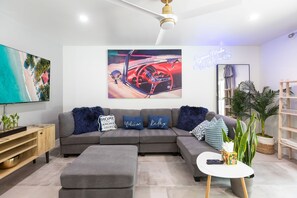 A modern living room with a sectional sofa, a flat-screen TV, and a large painting of a car.