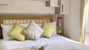 Una cama bien hecha con tres almohadas, una toalla doblada y un cabecero con panel de madera.