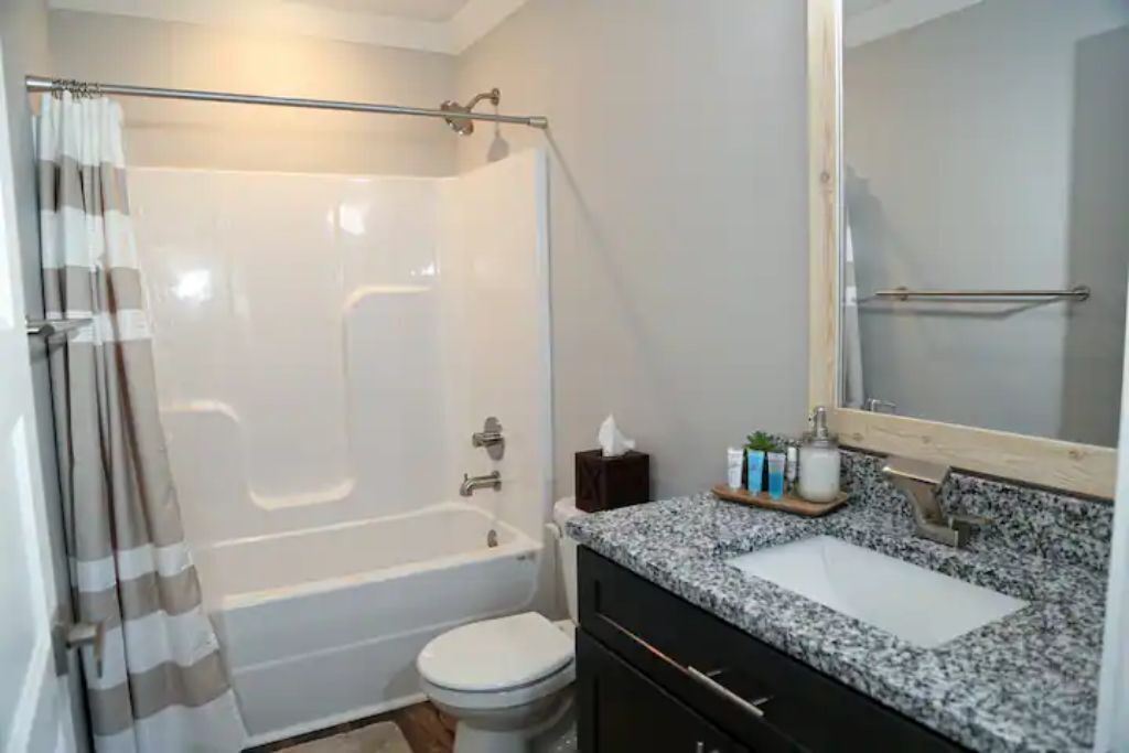 A bathroom with a shower, toilet, sink, and a mirror.