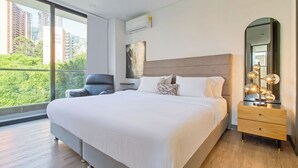 A modern bedroom with a large bed, a chair, a vanity with a mirror, and a city view. - Poblado Paradise for Your Stay 2br 2bath (Medellín)