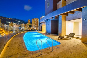 A rooftop pool with a clear view of the city skyline and mountains in the background.