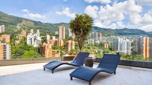 A rooftop terrace with two lounge chairs and a small tree, overlooking a cityscape with high-rise buildings and mountains. - Poblado Paradise for Your Stay 2br 2bath (Medellín)