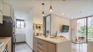 A modern kitchen with wooden cabinets, a central island, pendant lighting, and a view of greenery outside. - Poblado Paradise for Your Stay 2br 2bath (Medellín)