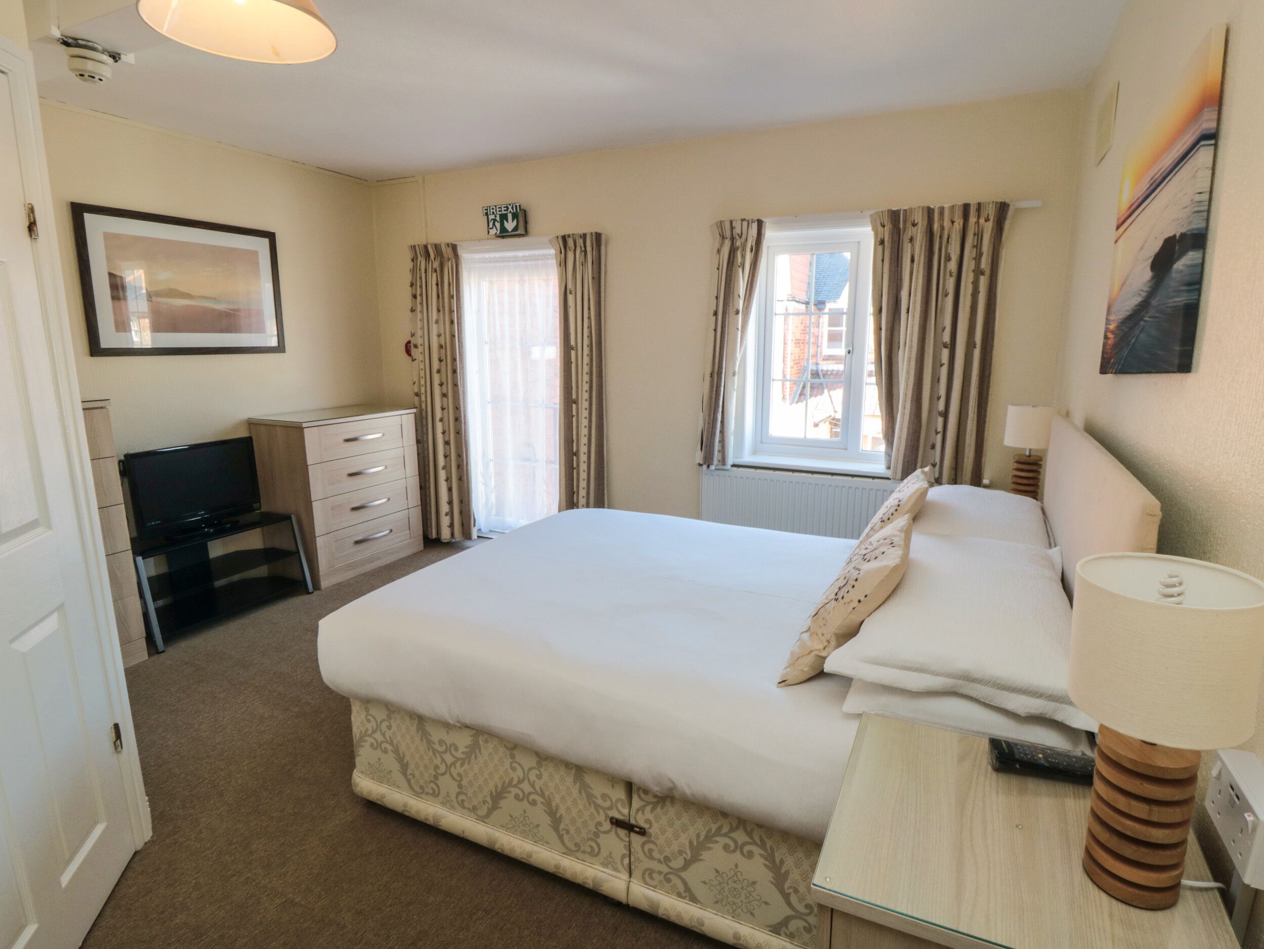 A hotel room with a large bed, a desk with a computer, a television, and a window with curtains.