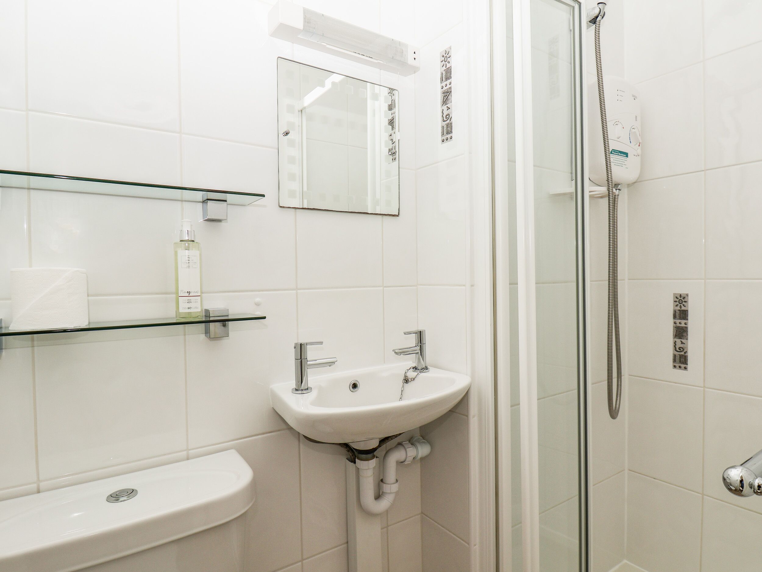 Ein modernes Badezimmer mit einer Duschkabine aus Glas, einem weißen Waschbecken und einem Spiegel darüber.