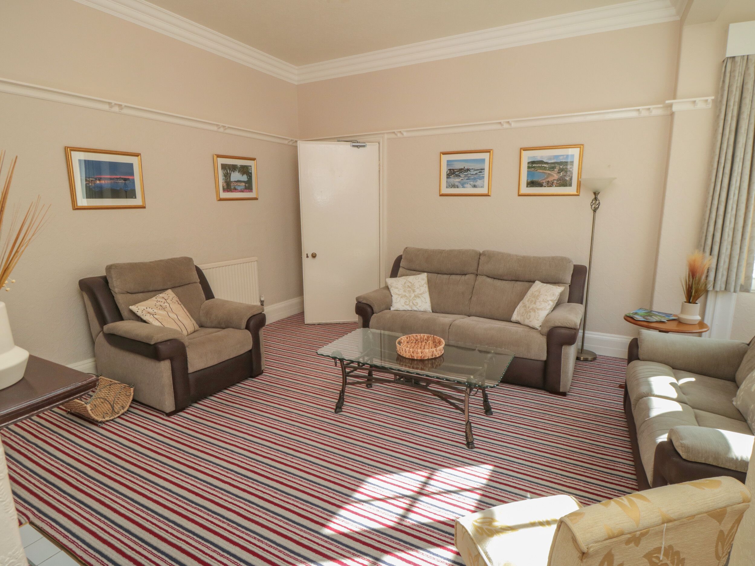 A living room with a striped carpet, two sofas, a glass coffee table, and framed pictures on the walls.