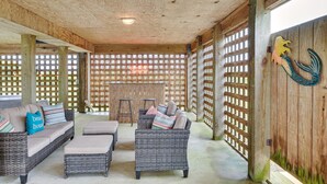 A covered outdoor seating area with wicker furniture and a wooden fence. - Nags Head Vacation Rental w/ Hot Tub: Near Beach! (Nags Head)
