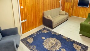 Una sala de estar con techo de madera, un sofá color beige, un sillón azul y un sillón verde, además de un tapete estampado.