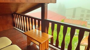 Una terraza de madera con una mesa, dos sillas, baranda y vista a edificios al fondo.
