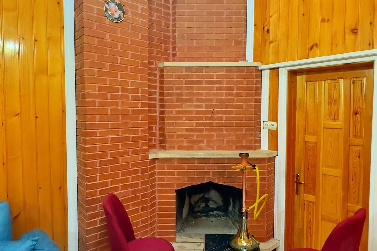 A room with a brick fireplace, two red chairs, a blue sofa, and a chandelier.