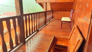 Un balcón de madera con una silla, una ventana pequeña y piso de madera.