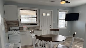 A kitchen with white cabinets, a stove, a sink, and a dining table with chairs.