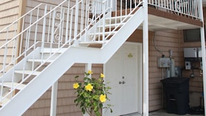 A two-story building with a white exterior, a covered porch, and a staircase leading to the upper floor.