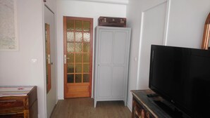 Una stanza con una porta in legno, un armadio, un televisore su un mobile in legno e un tavolino con un telecomando.
