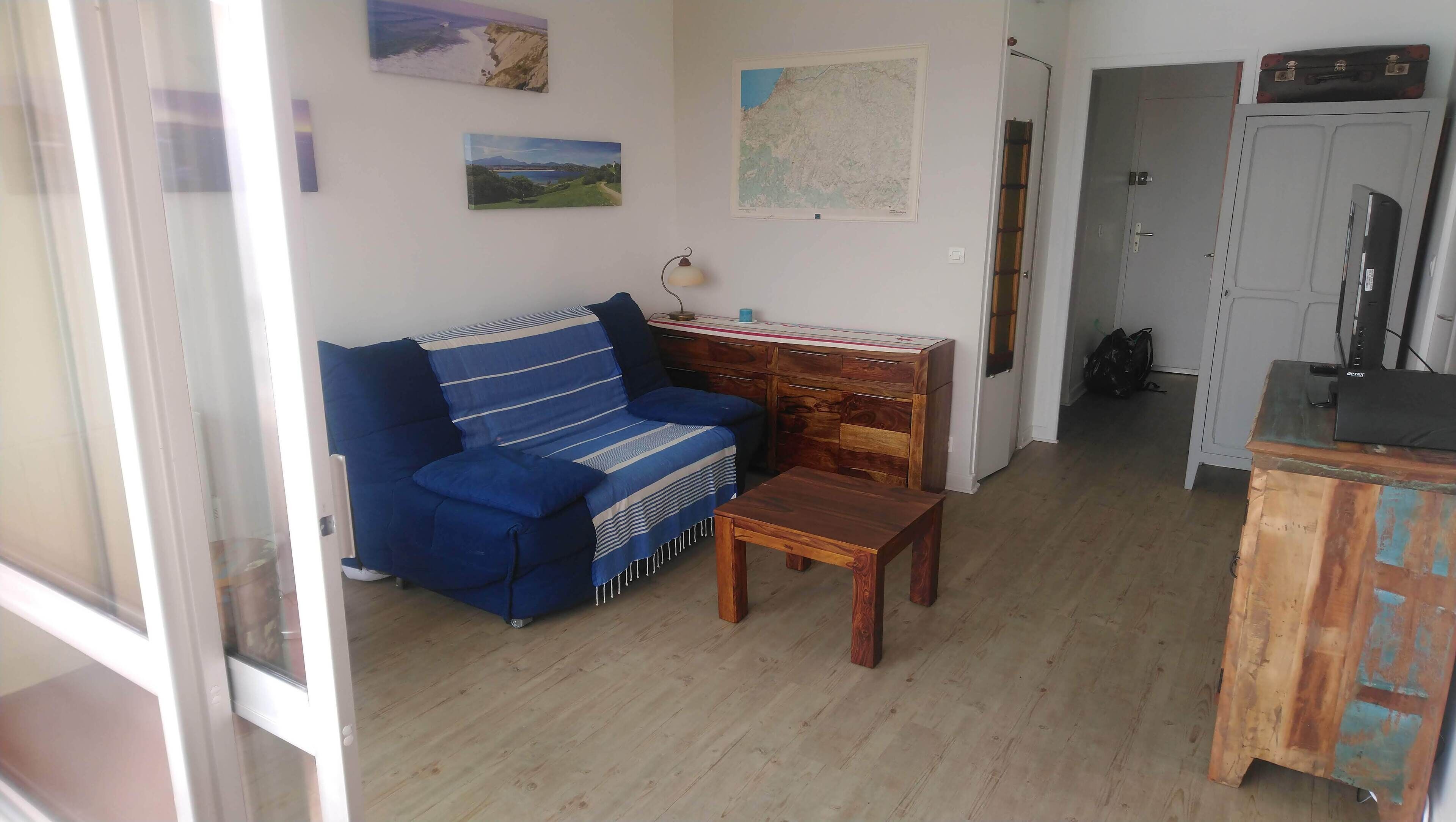 A room with a blue sofa, a wooden table, and a cabinet with a TV.