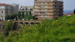 Un edificio a più piani con tetto piano, circondato da vegetazione e un ponte.