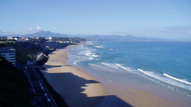 Una spiaggia con una strada che la costeggia, edifici sullo sfondo e cielo sereno.