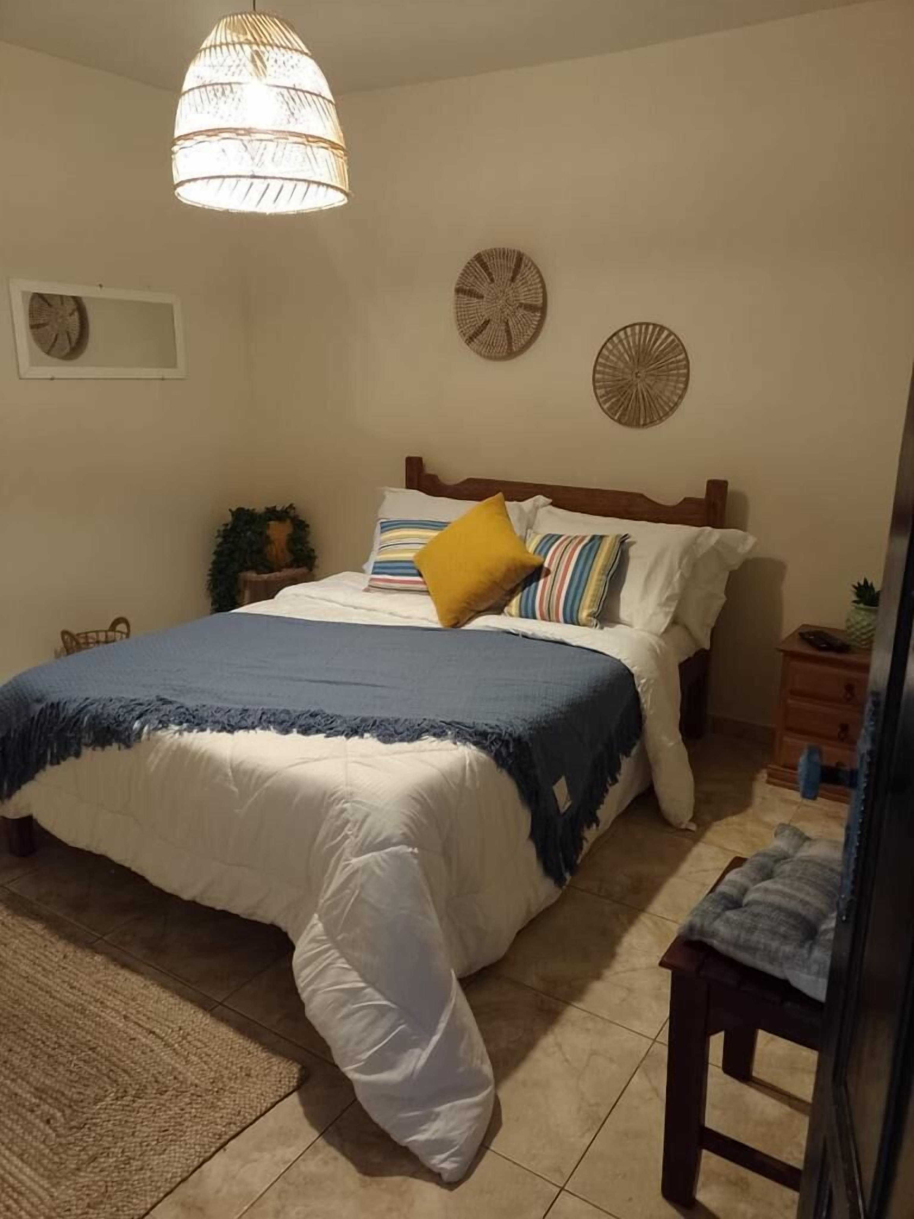 Un dormitorio con cama, mesitas de noche, lámpara colgante y decoración en la pared.