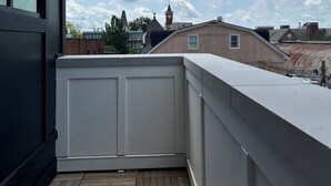 Ein Balkon mit Holzboden, der auf einen Wohnbereich mit Häusern und einem Glockenturm blickt.