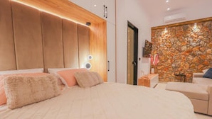Een moderne slaapkamer met een groot bed, houten hoofdbord, stenen muur en een klein zithoekje.