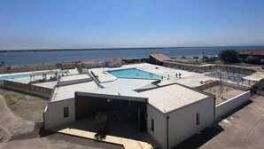 A rooftop pool area with a clear view of the sea, a covered seating area, and a small building with a door.