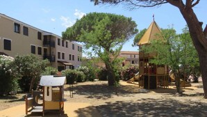 A playground with climbing structures and a small building, surrounded by trees and buildings.
