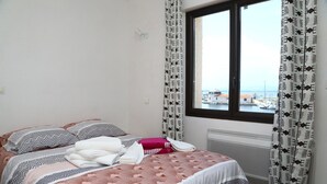 A hotel room with a bed, pillows, and a view of the sea through a window.