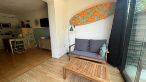 A living room with a sofa, a coffee table, and a surfboard decoration on the wall. - Le tinharé - studio with garden near the sea (La Ciotat)